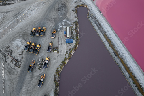 Aerial view of vibrant pink salt ponds contrasting with the industrial earth tones of machinery and land, Aigues, Occitanie, France.