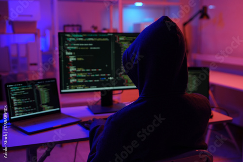 A mysterious hooded hacker working on a computer in a dark room.
