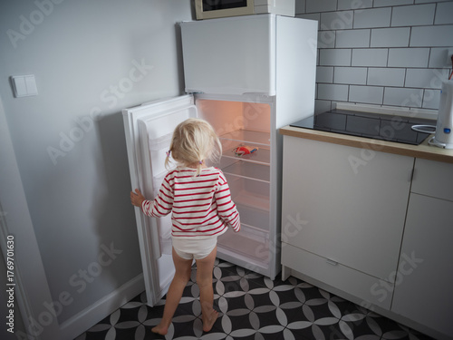 Little hungry girl looking into an empty refrigerator at home, no food concept