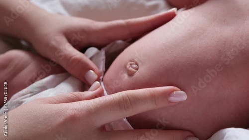 Loving mother's hands tenderly caressing and massaging her newborn baby's belly and navel to help with colic and digestion, showing a moment of care, love, and maternal connection