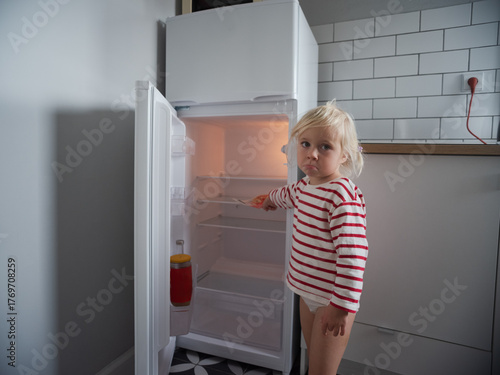 Little hungry girl looking into an empty refrigerator at home, no food concept