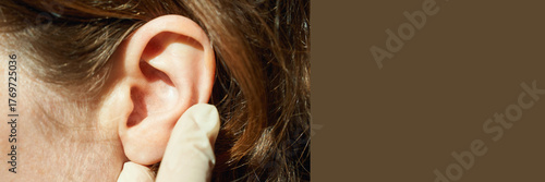 Female caucasian adult ear examined by gloved hand in medical checkup with brown hair visible.