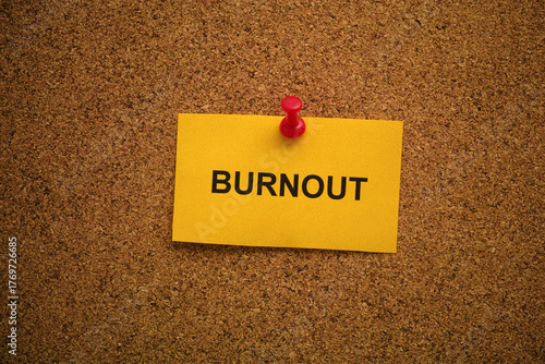 A yellow paper note with the word Burnout on it pinned to a cork board. Close up.