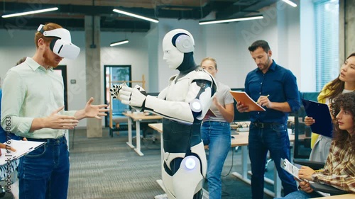 Man wearing VR headset interacting with humanoid robot. Group of colleagues writing observations and analyzing project performance. Focused team testing robotics development in technology workspace.