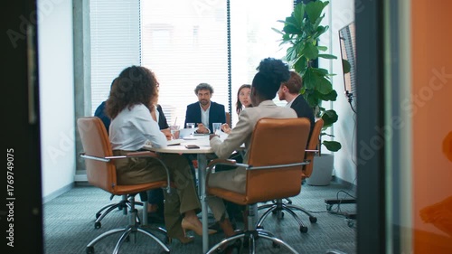 Team of professionals sitting around table discussing work problem. Man in center leading heated debate while colleagues sharing opinions. Collaboration and conflict resolution in meeting room.
