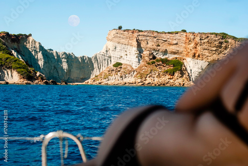 Woman on a luxury yacht in Greece. Mediterranean coastline with full moon over a cliff in the background. 