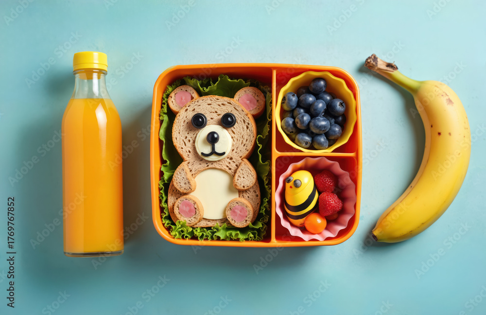 Fototapeta premium Funny bear sandwich, blueberries, strawberries, physalis, bee decoration in kids lunch box. Orange juice bottle, banana next to healthy school meal. Packed breakfast for children. Creative, fun, cute