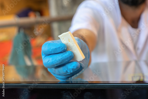 Hand offering a piece of white cheese in a market.