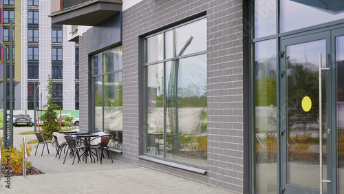 Fototapeta Naklejka Na Ścianę i Meble -  modern outdoor cafe seating area with empty tables and chairs on urban sidewalk. contemporary building design features large glass windows. inviting space for relaxation and socializing