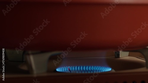 Compact portable gas stove with ignition, blue flame burning on kitchen gas burner, close-up view. The cook places a frying pan on the portable gas stove with the fire, preparing for cooking.
