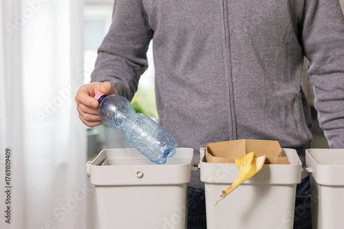 Individual recycling plastic bottle into bin while sorting waste at home, promoting sustainability and eco-friendly practices in daily life