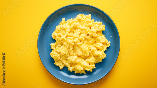 Scrambled eggs on a blue plate, against a yellow background, top view