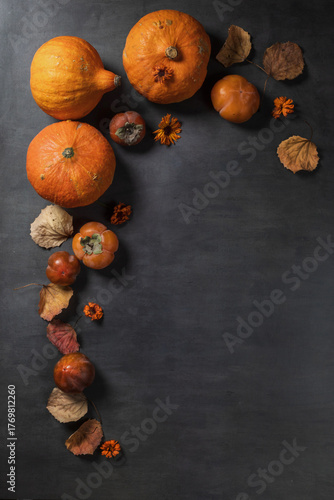 Autumn still life with pumpkins, dried leaves, and orange fruits against a dark abstract background.