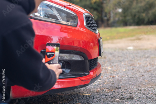 Man taking photo of damaged red car with smartphone. Rear view.