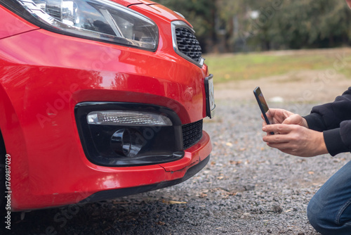 Man taking photo of damaged red car with smartphone. Rear view.