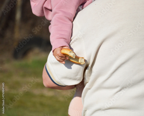 big bitten bagel in child's hand. adult man holds child in his arms. father and daughter. grandfather and granddaughter. snack during walk