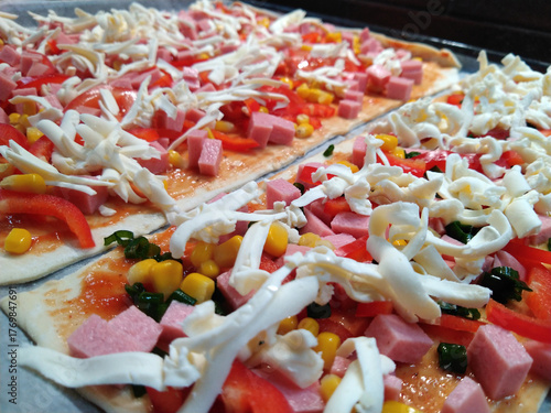 cooking delicious pizza with sausage, tomatoes and cheese at home close-up. ingredients for baking cheese, sausage, tomato sauce and tomatoes, corn, olives. delicious snack for children and adults