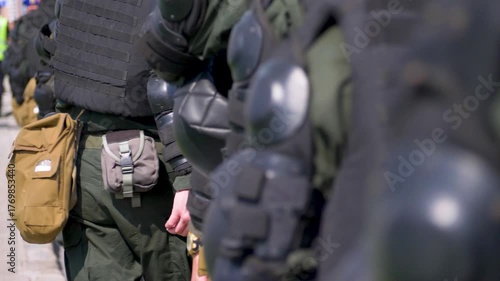 Riot gear pads, shield, uniforms highlight readiness for unpredictable protest. Group of uniformed officers stands united in public space. Police presence marks balance of authority and peace