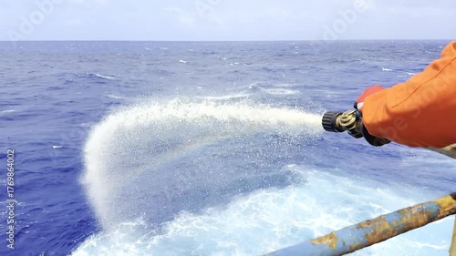 Crew tests fire hose on cargo ship, water flowing overboard during safety equipment drill at sea 2 Realistic view of maritime safety procedures and shipboard emergency preparedness.