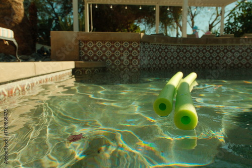 Close up of green pool noodles in a peaceful pool in a mansion on a sunny day