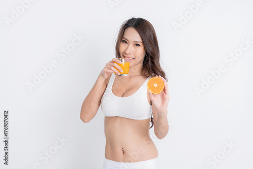 Attractive smiling Asian woman in a white bra and brief, hold orange and juice symbolizing health skincare and natural beauty at studio shot on white background.