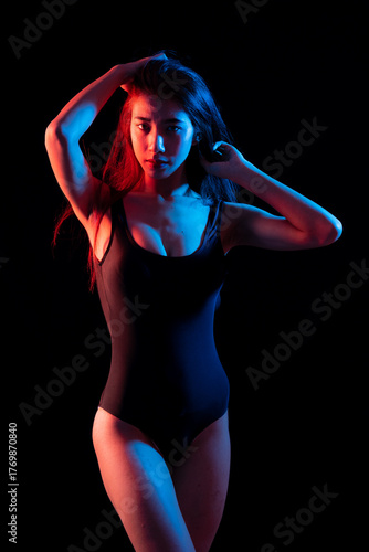 Fashion portrait striking image of a woman in a dark bathing suit, lighting color half lit in red and half in blue studio shot on black background.
