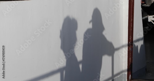 An intimate shadow of a couple cast on a white ferry wall, railing lines slicing through bright afternoon light. Minimal, anonymous and poetic—hinting at travel, closeness, and a quiet pause.