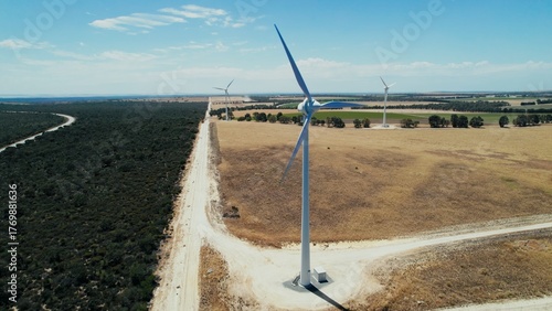 Wind turbines stand tall in a vast landscape of fields and trees under a clear blue sky during daytime