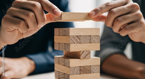 Careful hands place wooden block on unstable tower, representing strategy and risk