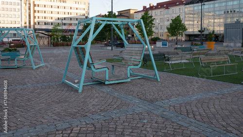 Public square with modern turquoise swings and benches in evening light