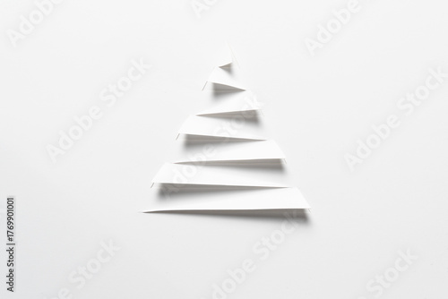 A minimalist white paper cut in a stepped, triangular shape to evoke a Christmas tree, with a striking background showing through the cuts, for Christmas celebration or simple winter themes.