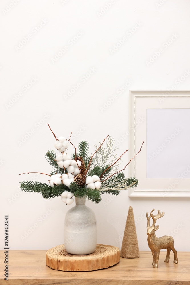 Fototapeta premium Beautiful composition with fir tree branches in vase and reindeer figure on wooden table near white wall indoors. Winter decor