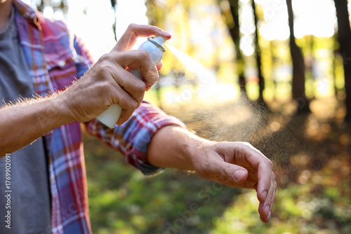 Man spraying tick repellent onto arm in park, closeup