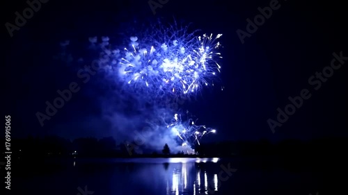 Brilliant blue fireworks illuminate the dark night sky, reflecting beautifully on the calm water below, creating a stunning nocturnal display.