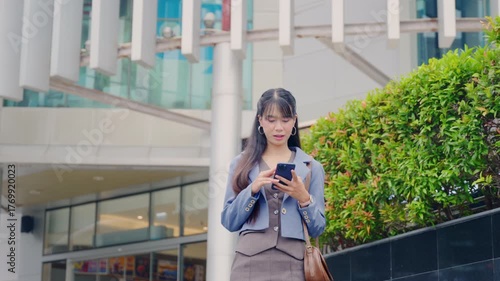 Young business businesswoman walking outdoor near modern office buildings, using mobile phone for travel, focused on technology communication on city street.