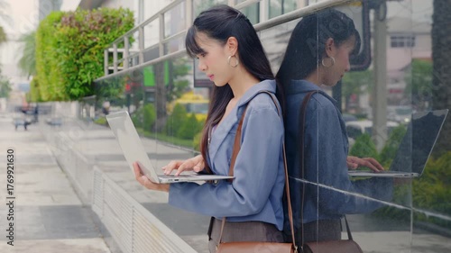 Young business businesswoman works on laptop outdoor near modern office building, focused professional manages project, cityscape reflects dynamic urban travel life.