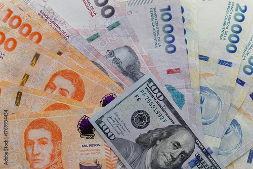 Bild auf Leinwand Argentine peso banknotes arranged in a fan covering the entire frame with a 100 US dollar bill placed on top, editorial concept illustrating inflation and exchange rate