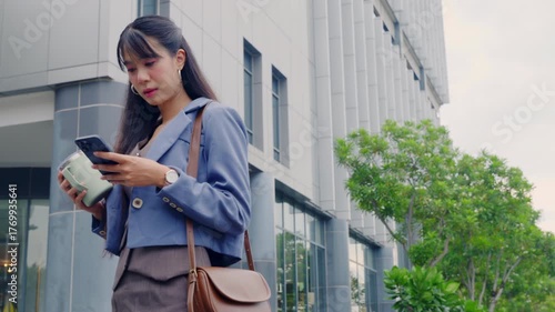 Young professional business businesswoman walking outdoors holding smartphone and travel mug, enjoying modern city travel near contemporary office architecture.