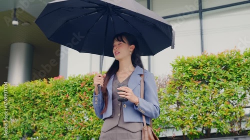 Young business woman walking outdoor, modern office district provides urban backdrop, holding umbrella and coffee cup, prepared for city travel or important meeting.