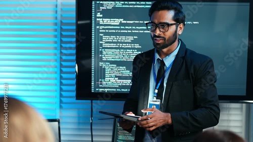 Professional man presenting software code on a screen in a modern office. Developer discusses programming, data security, or tech business strategy. Cybersecurity meeting with team