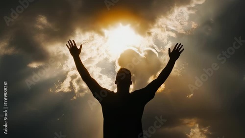 Silhouette of person with arms raised against cloudy sky with sun rays shining through clouds