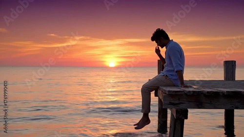 Indian Man relaxing on wooden pier while watching vibrant ocean sunset