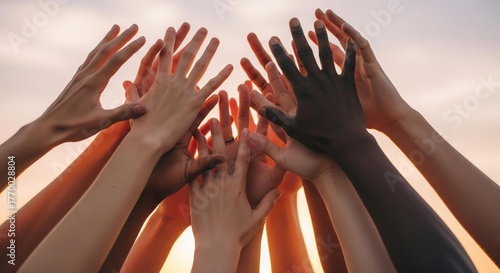 Diverse hands reaching up together, symbolizing unity, teamwork, and collaboration against a warm, sunset background.