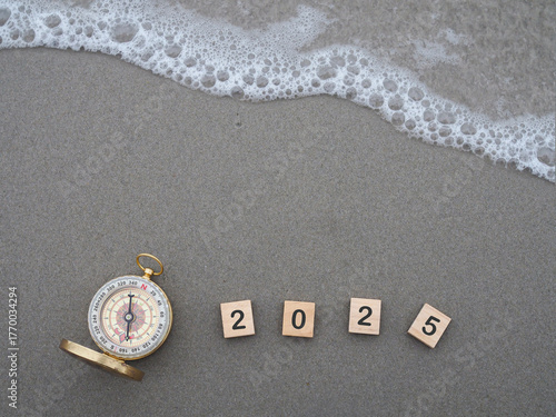 Wooden blocks with the number 2025 and Compass on the beach with ocean waves. The concept of world tourism day, Searching the right directions and Travel in year 2025