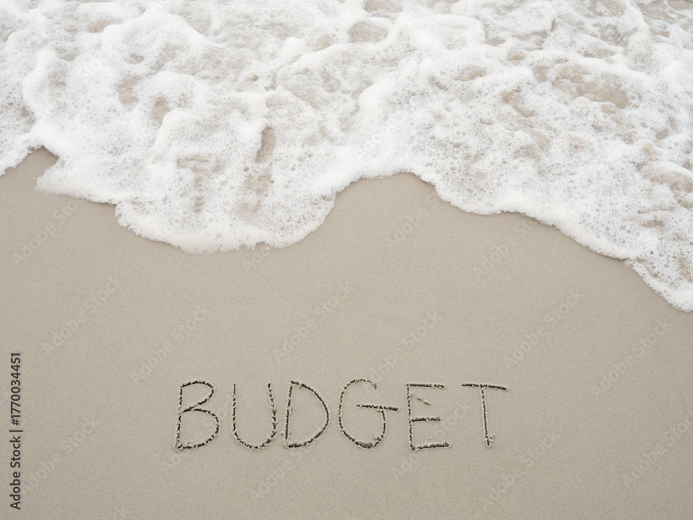 Fototapeta premium BUDGET handwritten with ocean waves on a sandy beach. The concept about budget planning and allocation