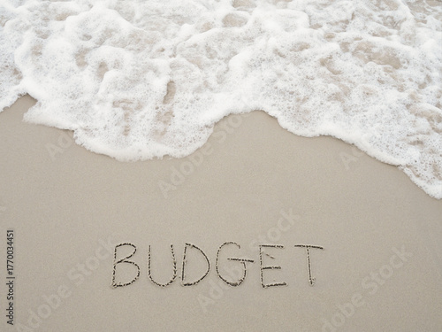 BUDGET handwritten with ocean waves on a sandy beach. The concept about budget planning and allocation