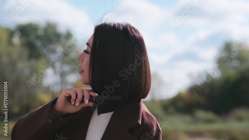a brunette woman brushed her hair in brown jacket outside near the river on nature. autumn atmosphere.