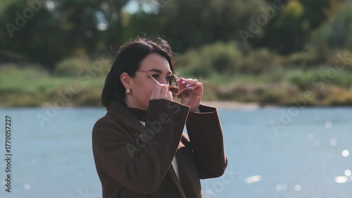 woman enjoying peaceful park walk near the river, casual autumn day with sunglasses and gentle wind movement