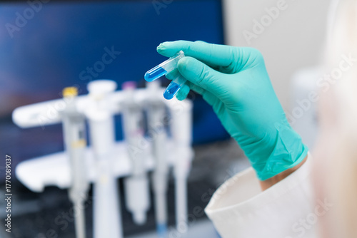 Female scientist in lab coat studying blue liquid in test tube used for DNA analysis and biochemical research.