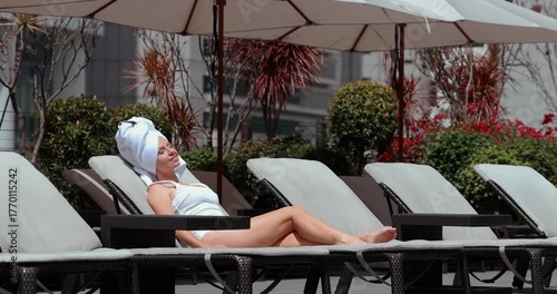 Woman relaxing on sunbed by poolside, urban hotel. Concept of leisure, luxury, summer vacation, outdoor relaxation, lifestyle.